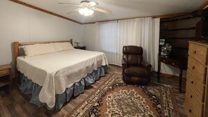 Un dormitorio con cama, ventilador de techo, una silla, cómoda y ventana con cortinas.