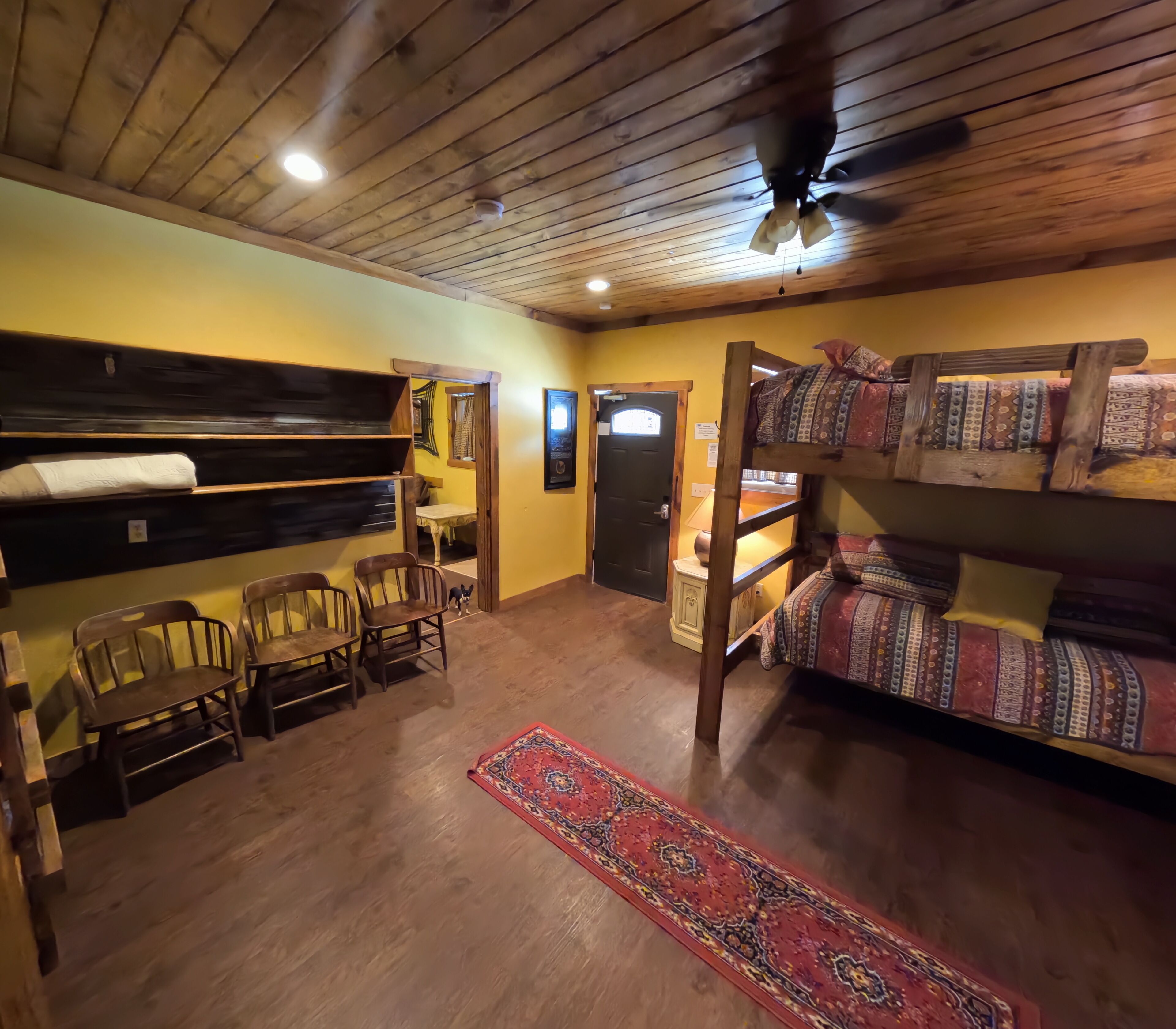 A room with bunk beds, a dining table with chairs, a red patterned rug, and a ceiling fan.