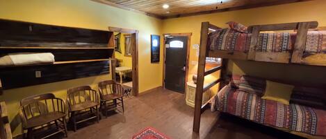 A room with bunk beds, a dining table with chairs, a red patterned rug, and a ceiling fan.