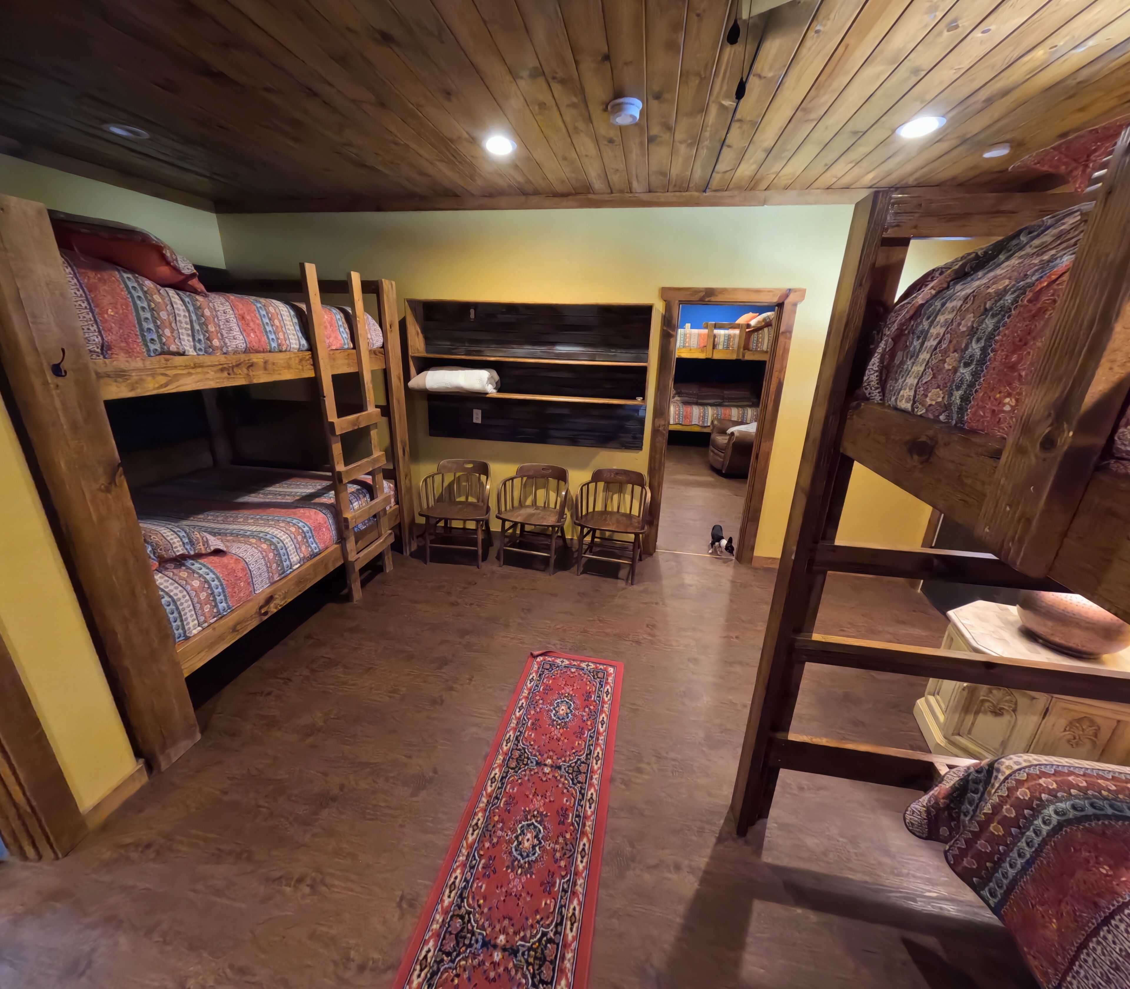 Une chambre rustique avec des lits superposés en bois, un tapis rouge à motifs et une petite table avec des chaises.