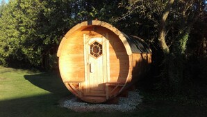 A wooden cylindrical structure with a hexagonal window and a door, surrounded by trees and grass. - Peach of a private beach! Waterfront cliff cottage near Bayfield (Zurich)