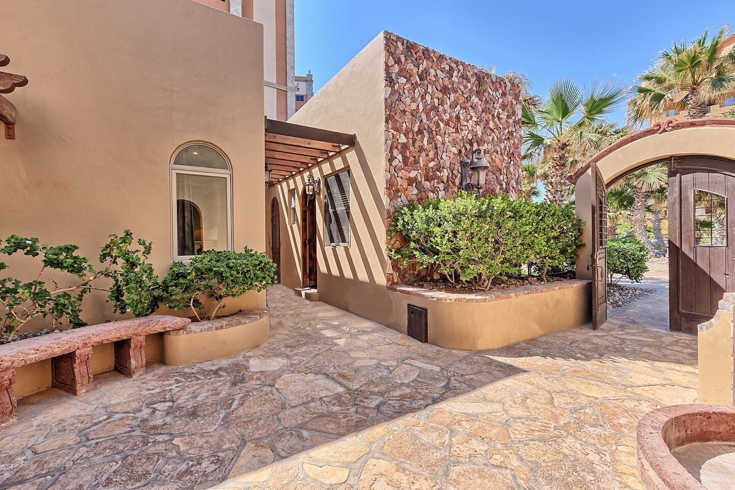 A courtyard with stone flooring, a wooden bench, and a wall with a mosaic pattern.
