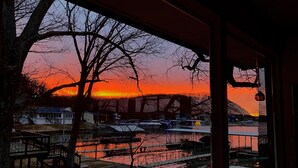 Vista del atardecer desde un espacio exterior cubierto, con un puente de metal al fondo.