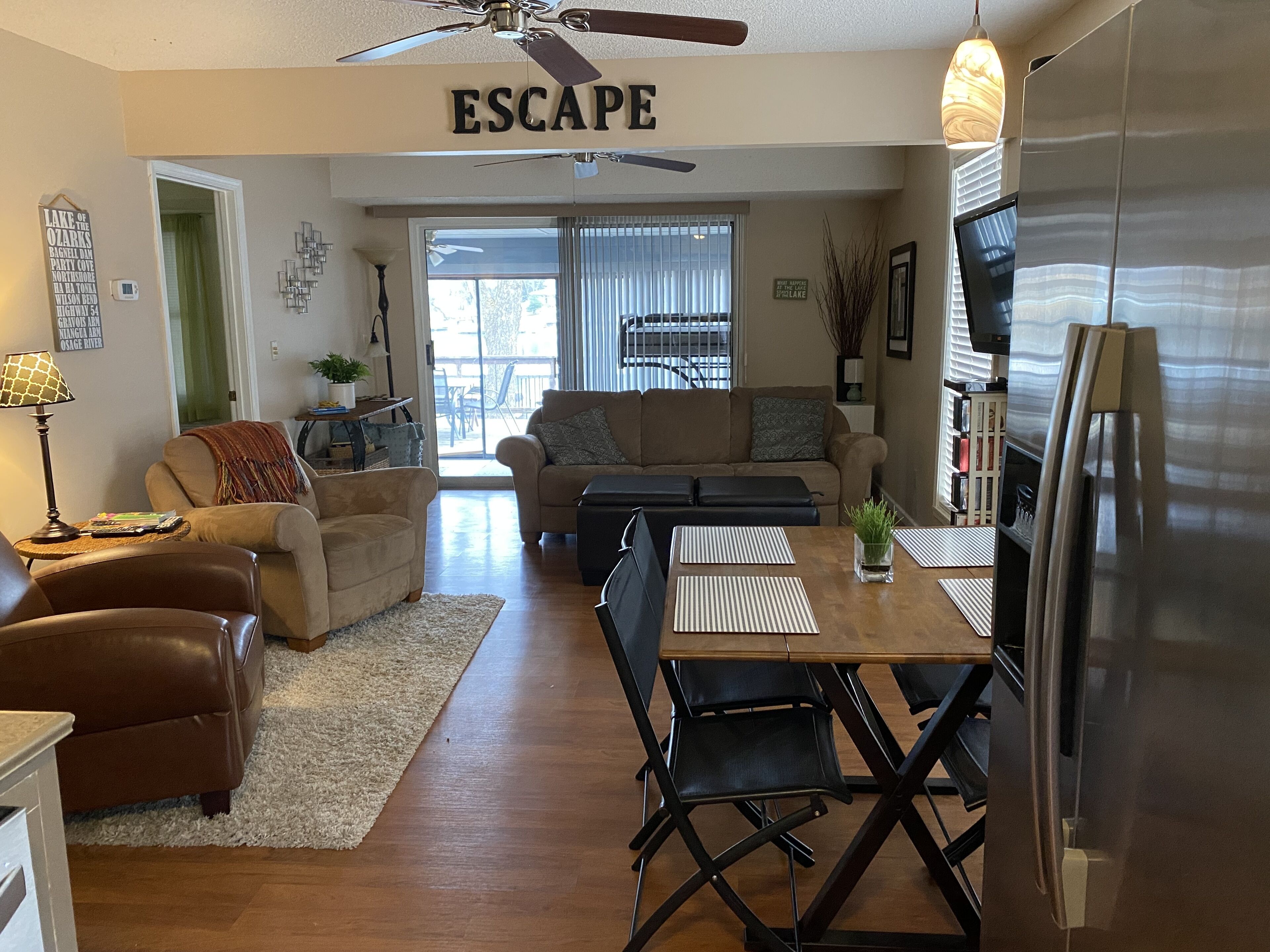 A spacious living room with a dining area, a ceiling fan, and a large refrigerator.