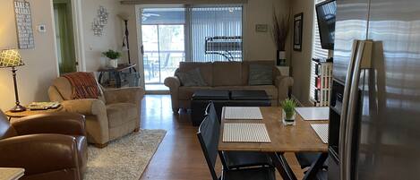 A spacious living room with a dining area, a ceiling fan, and a large refrigerator.