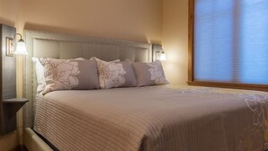 Una cama bien hecha con cubrecama acolchado y almohadas decorativas, flanqueada por mesitas de noche con lámparas de pared.