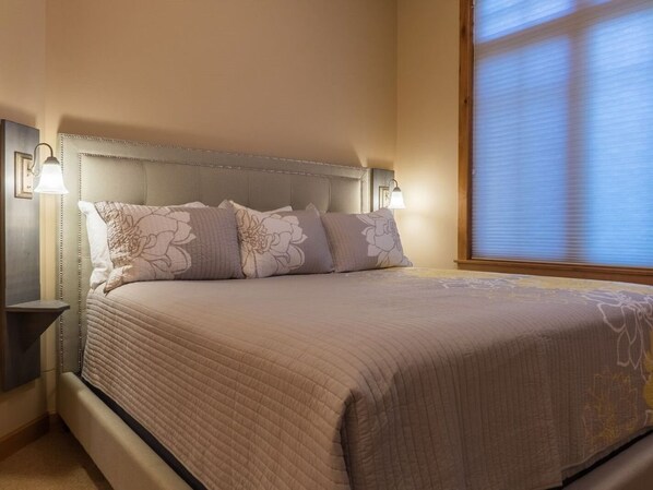 A neatly made bed with a quilted cover and decorative pillows, flanked by bedside tables with wall-mounted lamps.