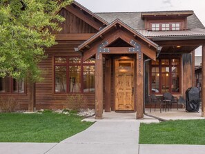 A wooden cabin with a prominent front door, a covered porch, and a small outdoor seating area. - Bridger Creek Luxury near Bozeman & Bridger Bowl Skiing - Legends Chalet (Bozeman)