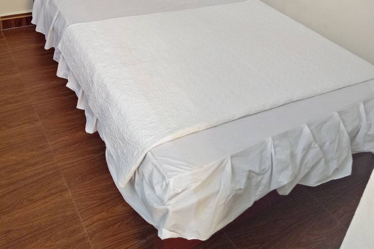 A single bed with white bedding and a headboard, a wooden floor, and a wall-mounted mirror.