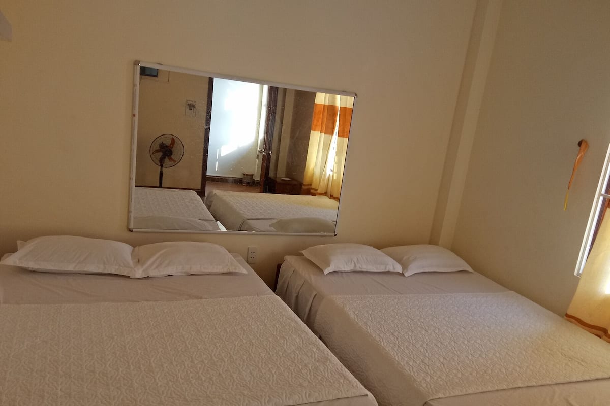 A hotel room with two single beds, a large mirror, and a standing fan.