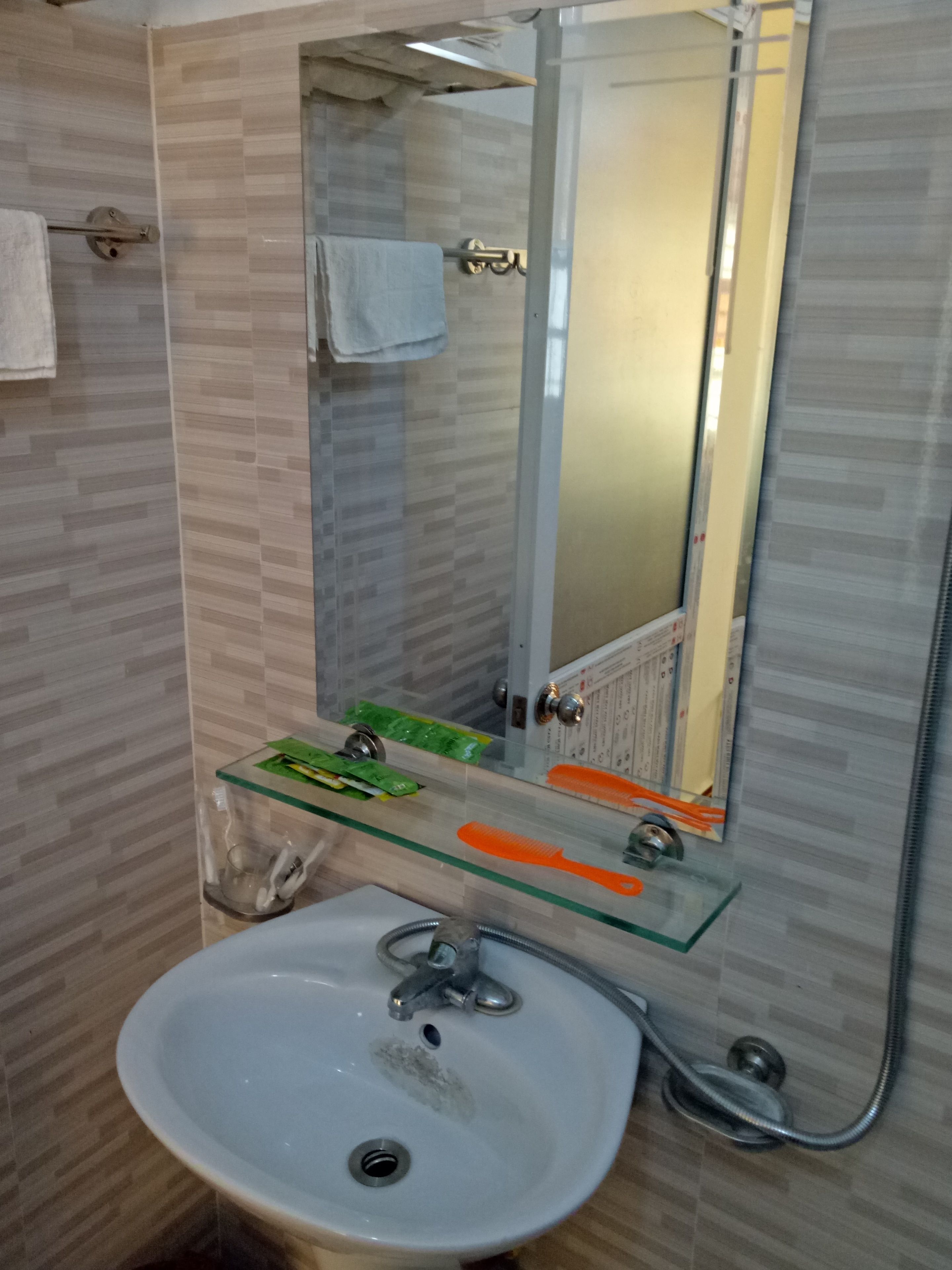 Een badkamer met een glazen plankje voor toiletartikelen, een witte wastafel met kraan en een spiegel erboven.