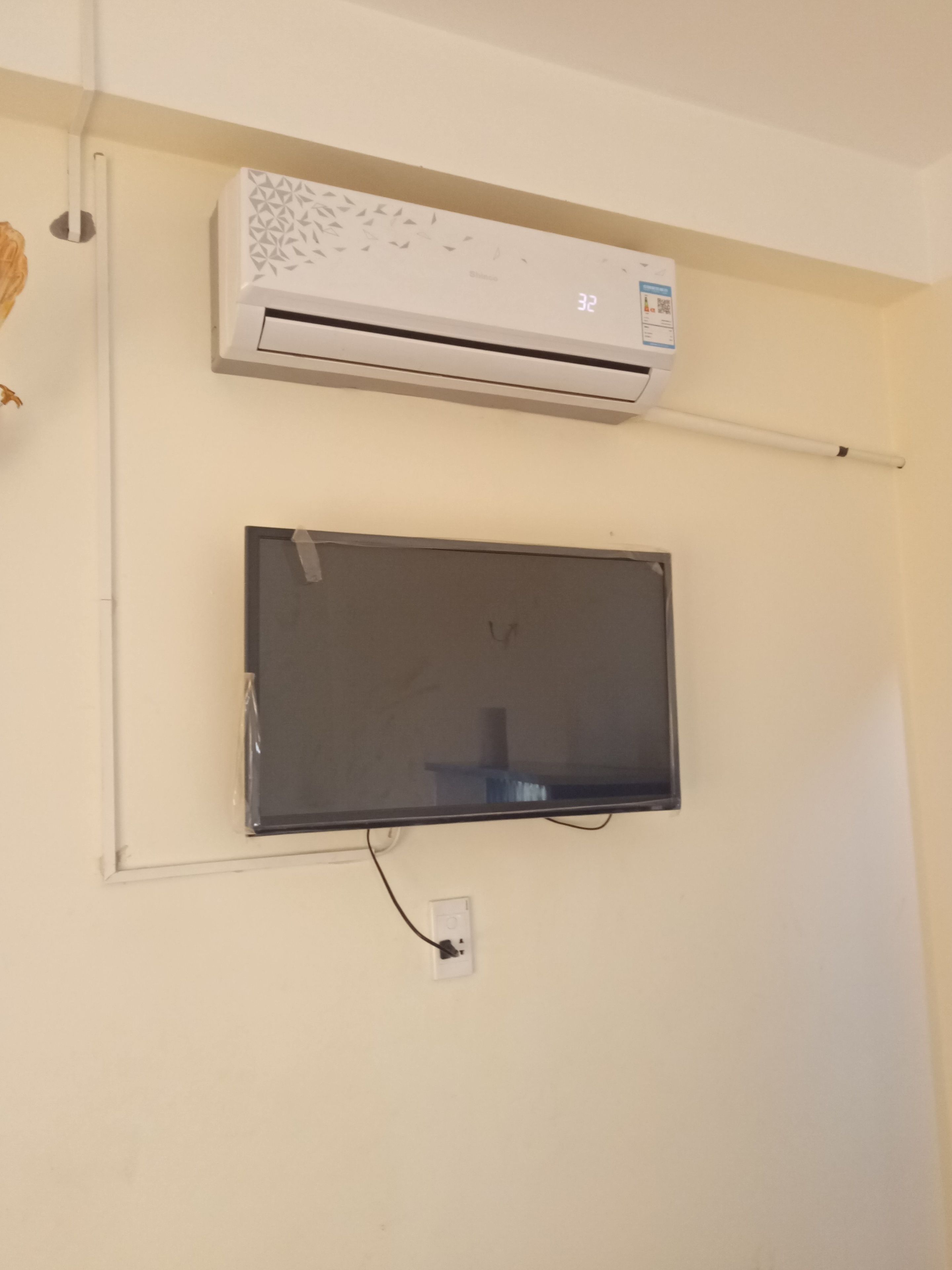 An air conditioning unit mounted on a wall with a flat-screen TV below it.