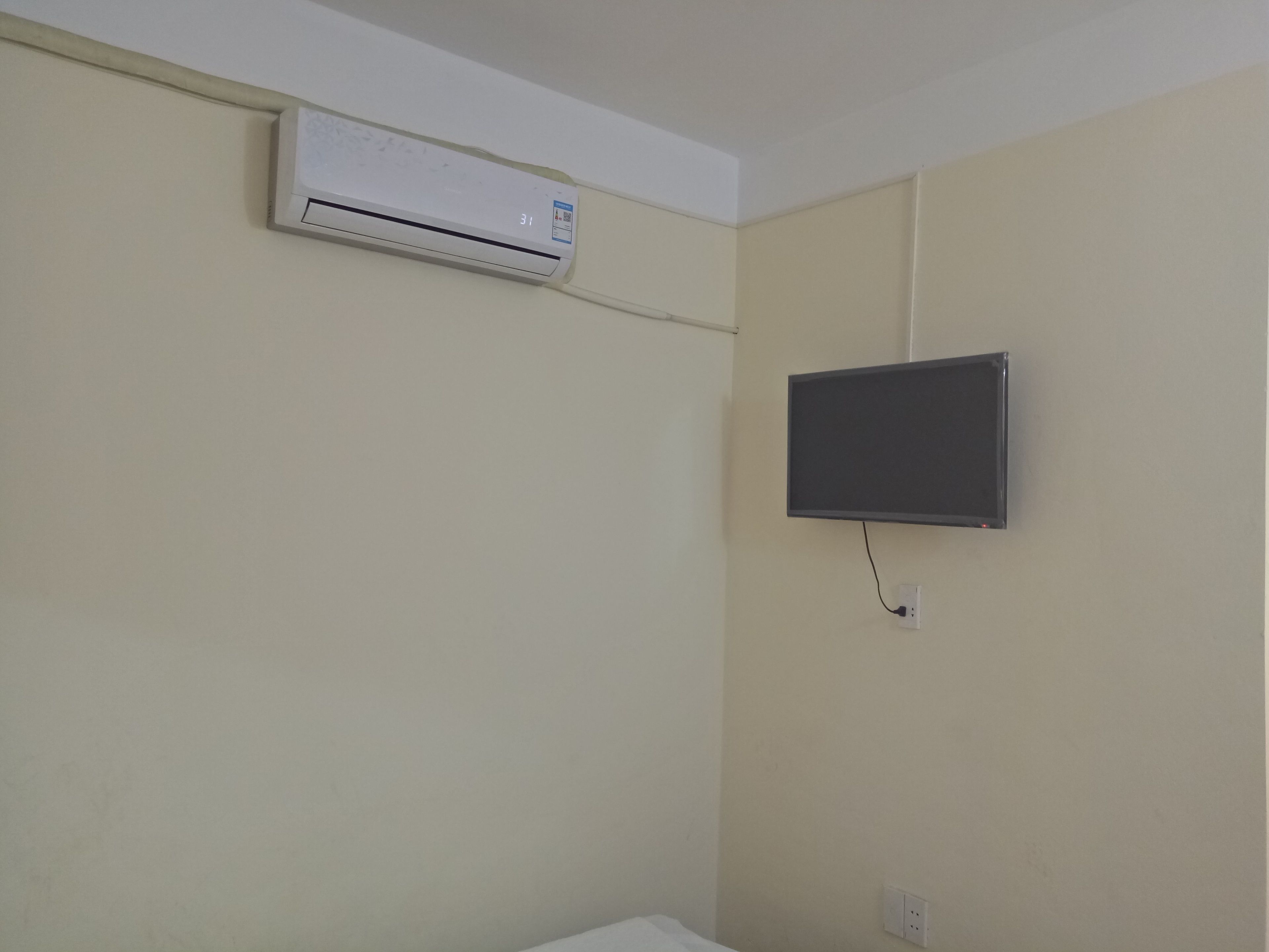 A room with a mounted air conditioner, a flat-screen TV, and a power outlet on the wall.