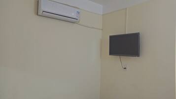 A room with a mounted air conditioner, a flat-screen TV, and a power outlet on the wall.
