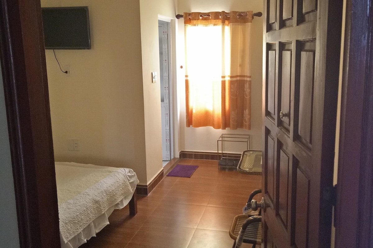 A room with a bed, a chair, a small table, a door, and a window with curtains.