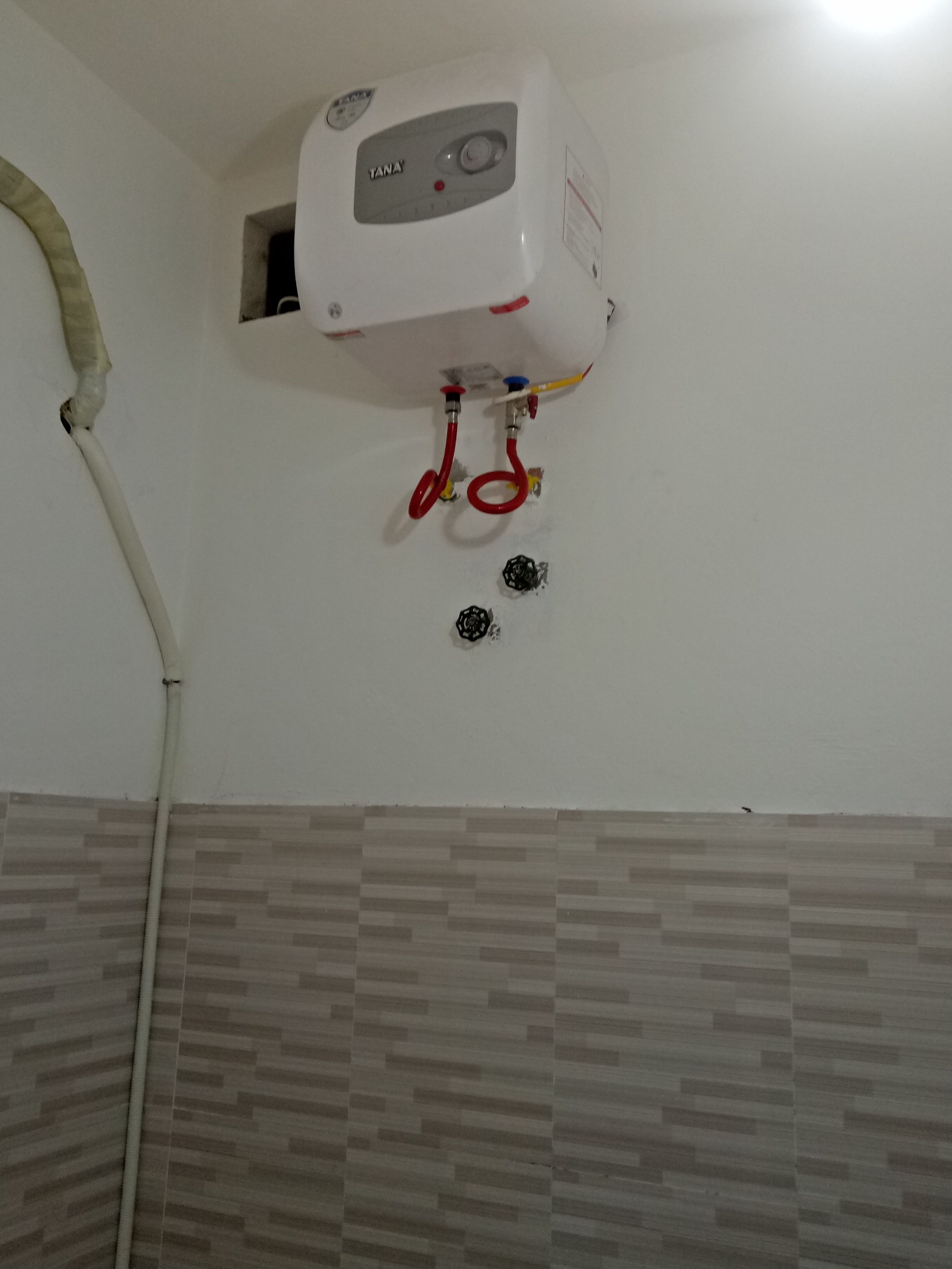 A white water heater mounted on a wall with a control panel, two red valves, and a white pipe.