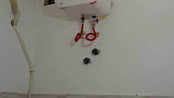 A white water heater mounted on a wall with a control panel, two red valves, and a white pipe.