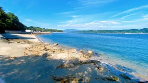 Une plage avec une eau d’un bleu limpide, un rivage sablonneux et des zones rocheuses.