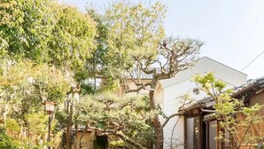 Un jardin japonais traditionnel, avec un sentier de pierres, des rochers recouverts de mousse et un bâtiment en bois doté de portes coulissantes.