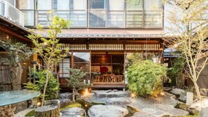 Un jardin de style japonais traditionnel, avec un bâtiment en bois, des allées pavées de pierres et diverses plantes.
