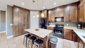 Una cocina moderna con armarios de madera, una isla central, taburetes de bar, un bote de basura y una cafetera.