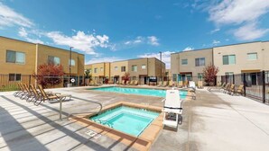 Zona de piscina con sillones de descanso y un jacuzzi pequeño, rodeada de edificios modernos.