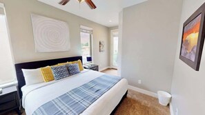 Un dormitorio con cama, mesitas de noche, ventilador de techo y cuadros en las paredes.
