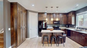 A modern kitchen with dark wood cabinets, a central island with stools, and pendant lighting. - Entrada at Moab - 430, Brand New 4 Bedroom Luxury T (Moab)
