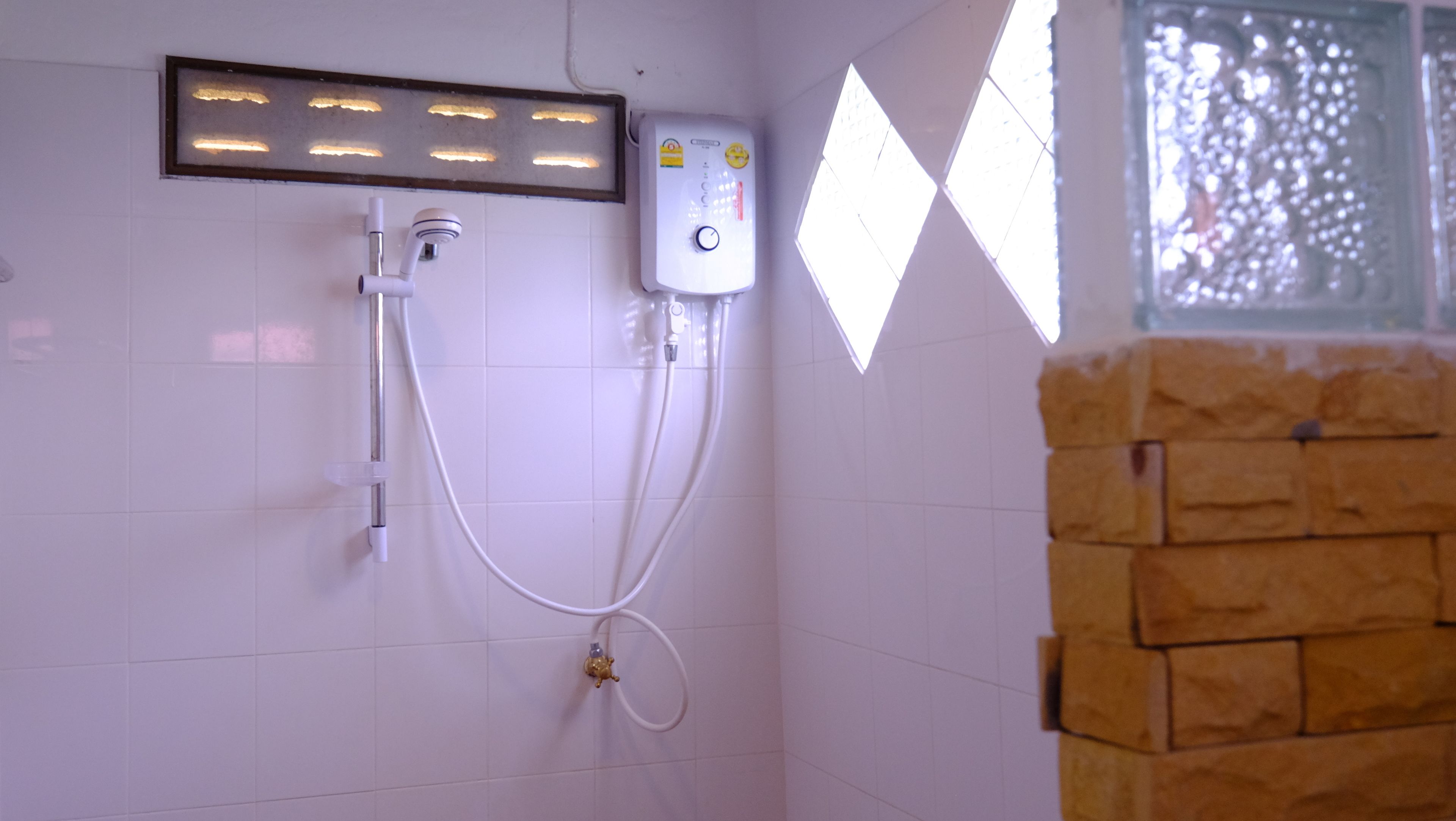 Baño con ducha, calentador de agua y ventana con celosía decorativa.