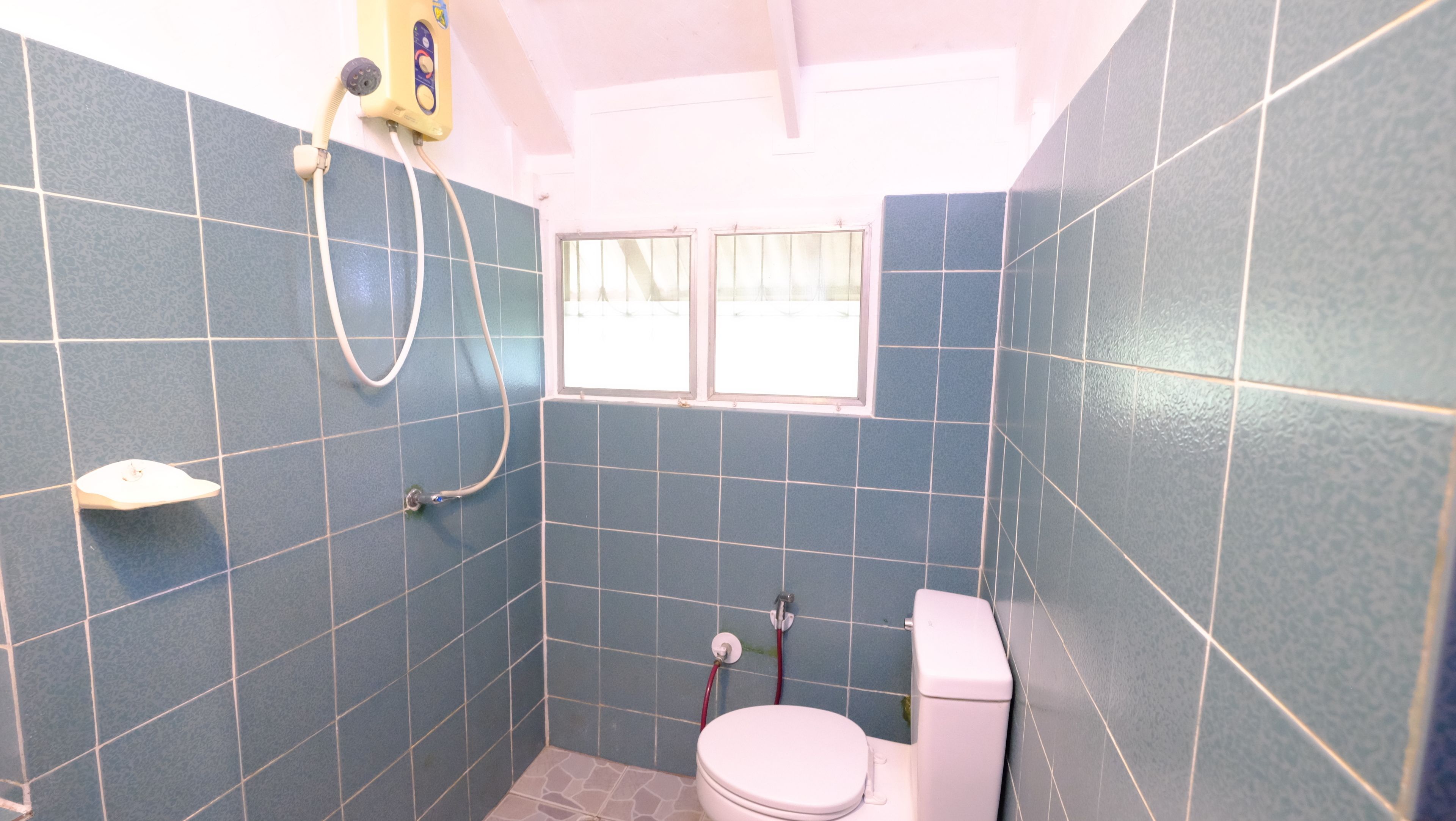 Un baño pequeño con azulejos azules, un inodoro, una ducha y un ventanal.