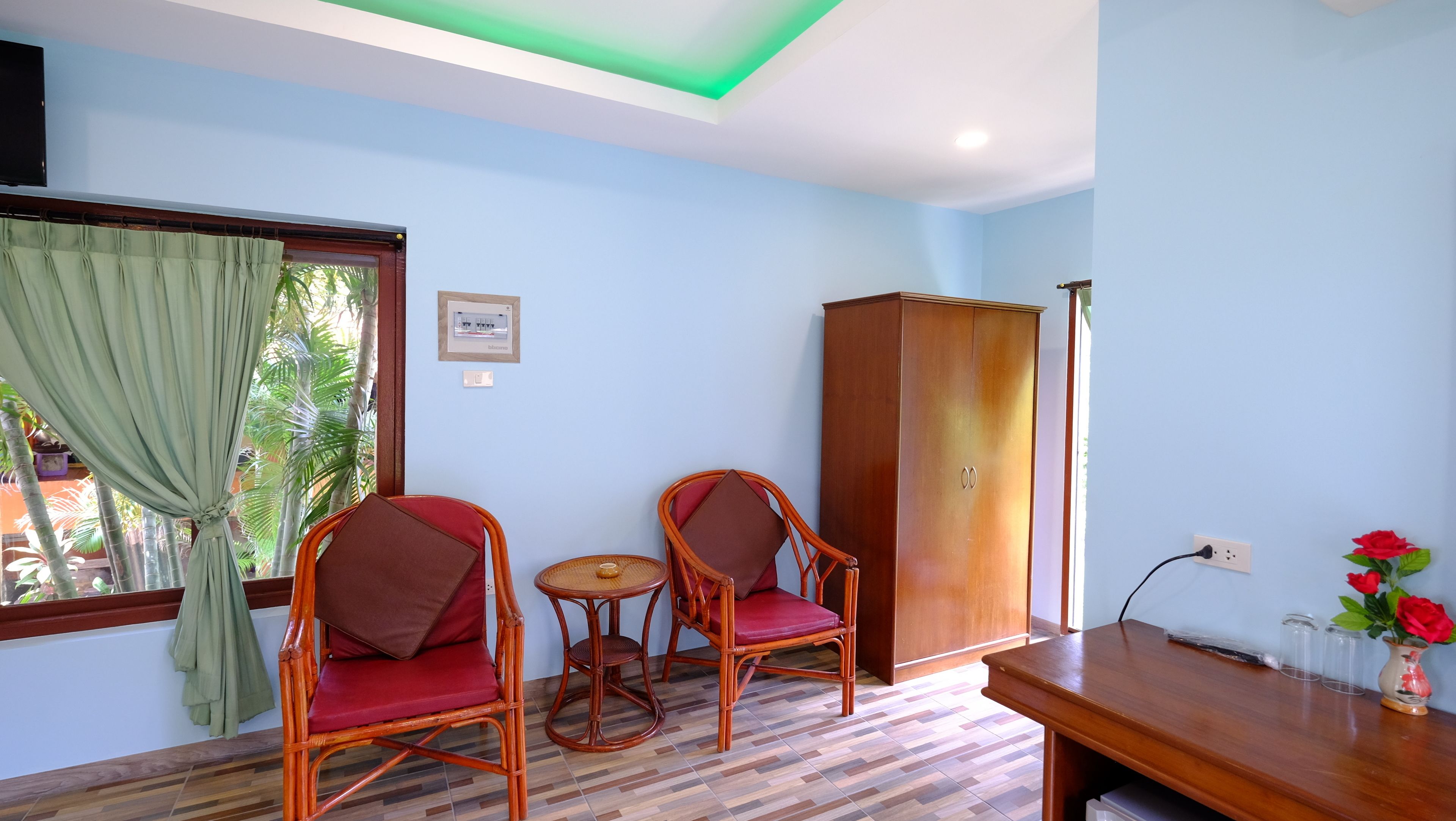 Una habitación con dos sillones de mimbre, una mesita, un armario de madera y una ventana con cortinas.