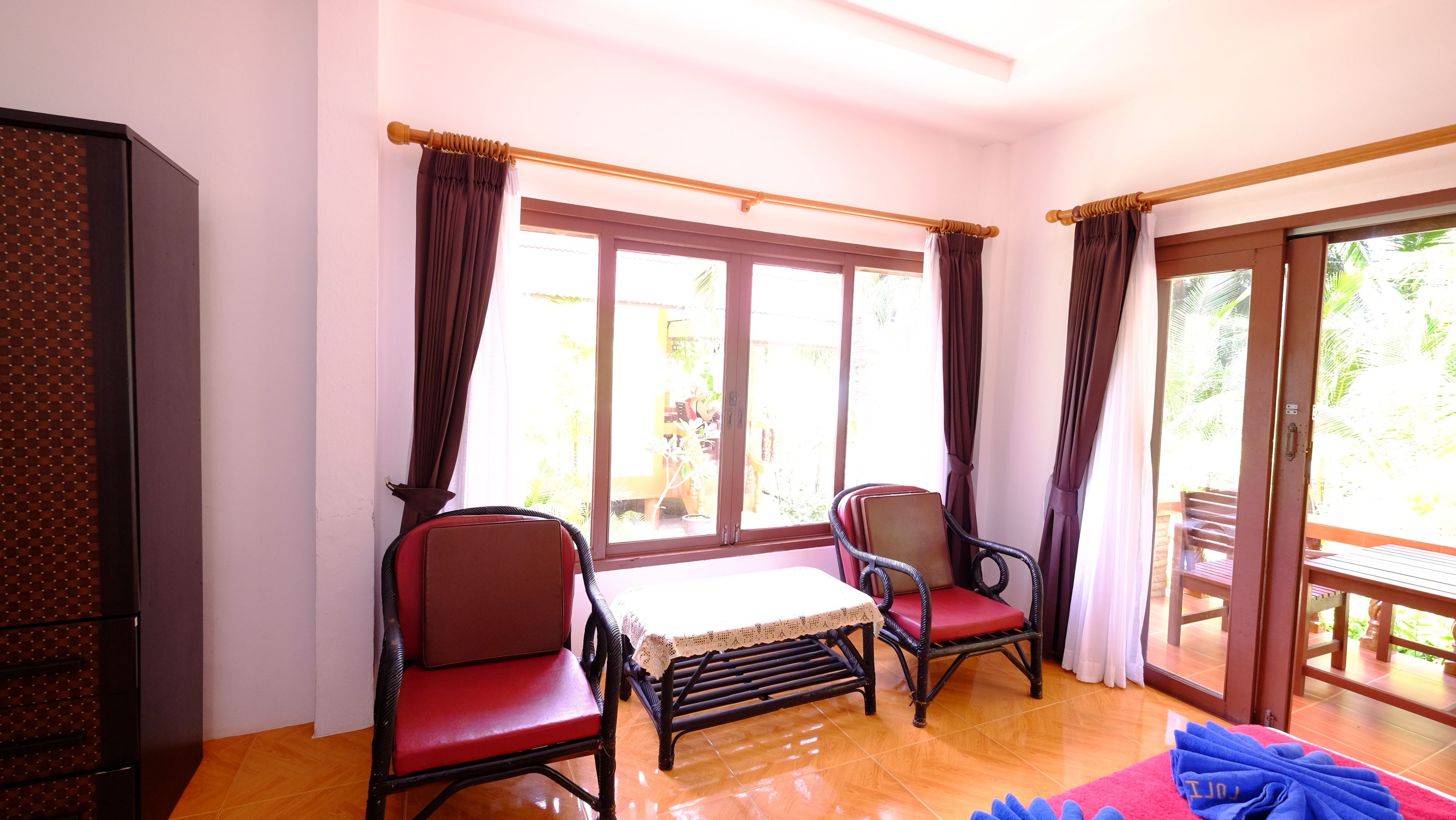 A room with two wicker chairs, a small table, and a view of the outdoors through large windows.