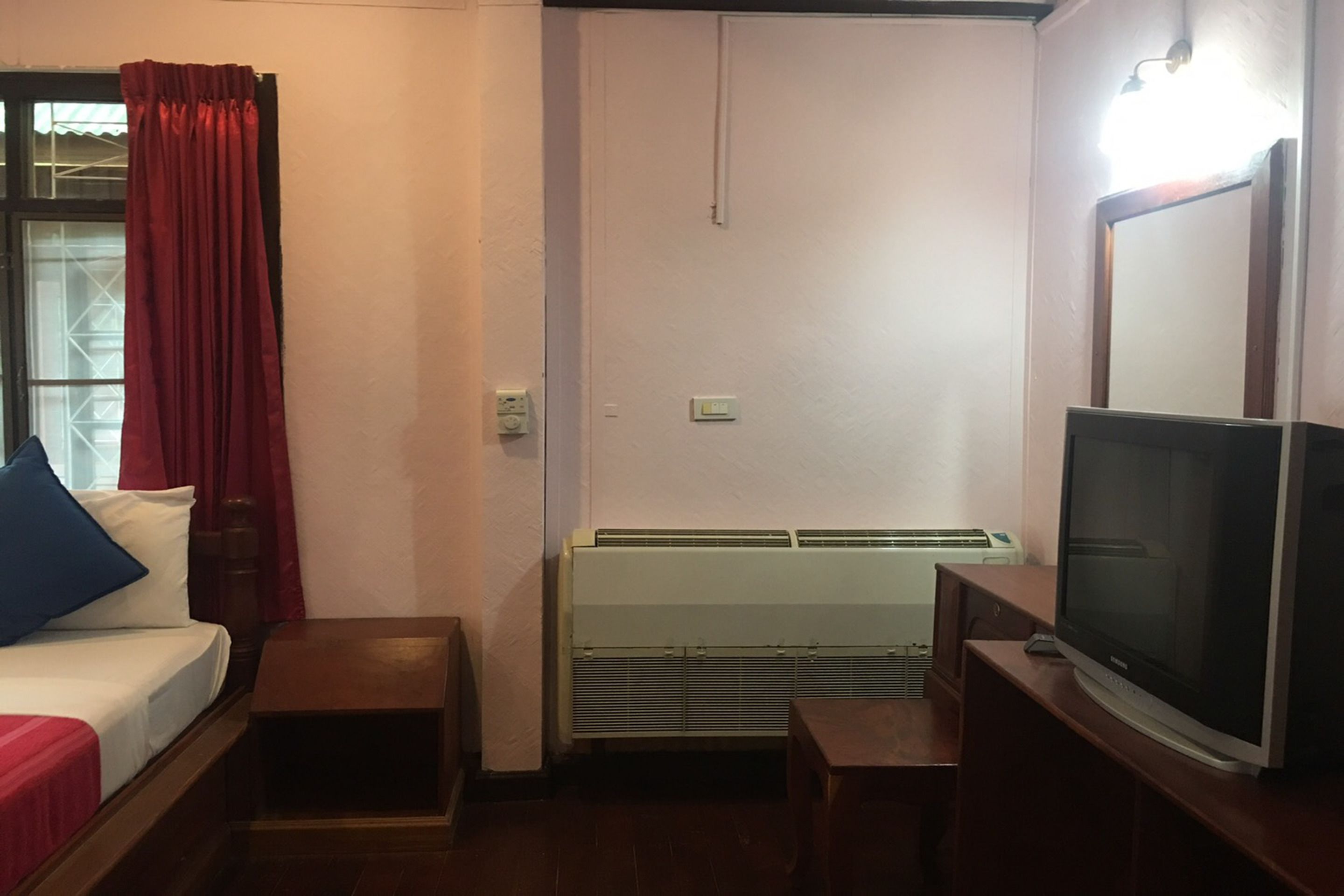 A compact hotel room with a bed, a small table, a TV, and a heater.