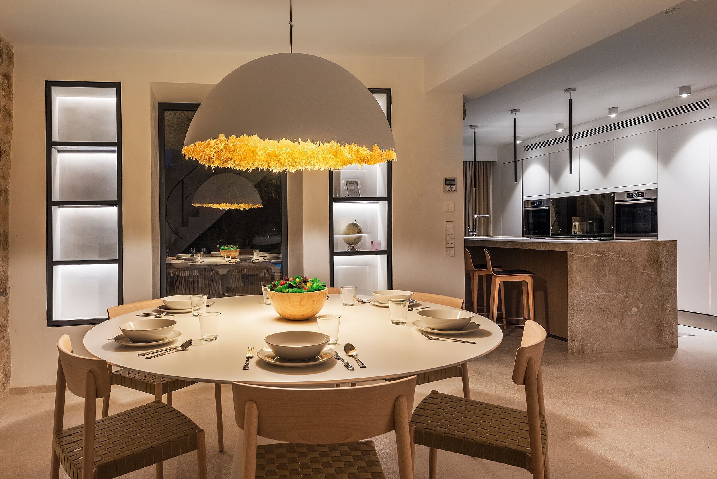 A modern dining area with a round table, chairs, and a central light fixture.