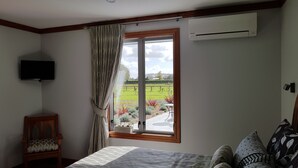 A bedroom with a bed, a TV mounted on the wall, a window with curtains, and an air conditioning unit. - BRUNTWOODLODGE - Adults Only (Tamahere)