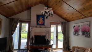 A living room with a fireplace, a television, and a chandelier. There are two doors leading to a garden. - BRUNTWOODLODGE - Adults Only (Tamahere)