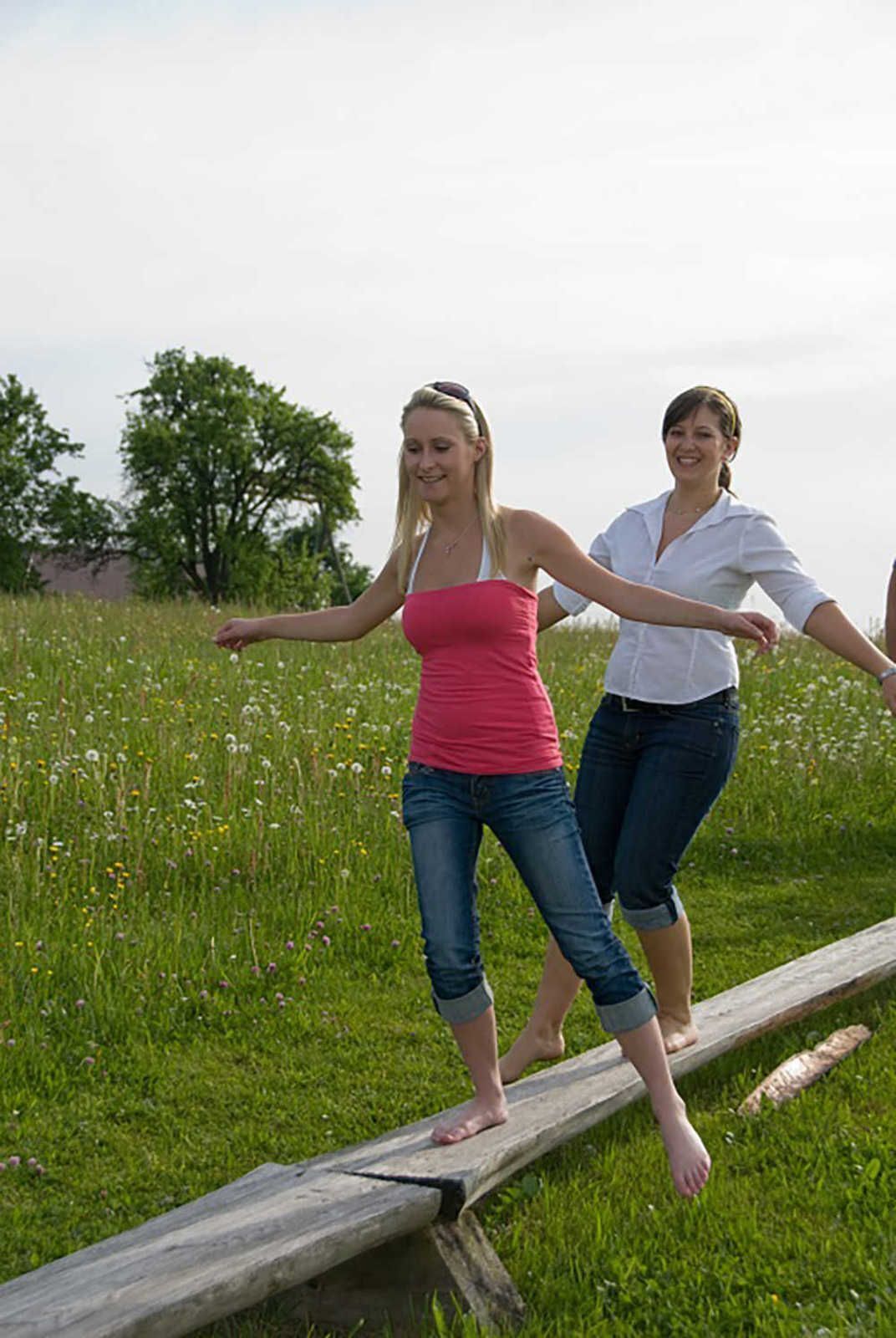 Twee personen lopen over een houten brug in een grasveld, met bomen op de achtergrond.