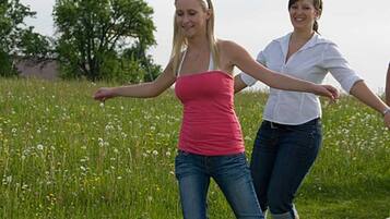 Twee personen lopen over een houten brug in een grasveld, met bomen op de achtergrond.