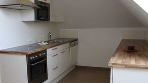 Uma cozinha com bancada de madeira, armários brancos, fogão e micro-ondas.