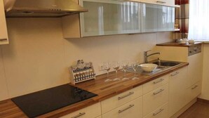 Eine Küche mit einem schwarzen Induktionskochfeld, weißen Schränken, einer Spüle aus Edelstahl und einem Fenster mit Vorhängen.