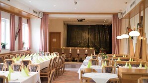 Ein Restaurant mit langen Tischen und Stühlen, einer Bühne im Hintergrund und einem großen Gemälde an der Wand.