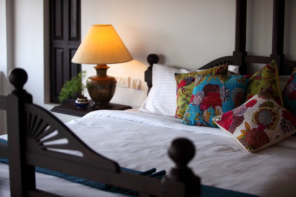 Een net opgemaakt bed met kleurrijke kussens en een lamp op een nachtkastje.