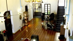 A spacious room with a patterned floor, a chandelier, a scooter, and a staircase leading to another level. - Waterfront Granary A Museum Hotel (Kochi)