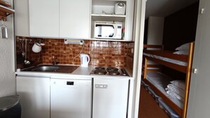 A compact kitchenette with a microwave, kettle, and stove. There is a sink and a small refrigerator. A bunk bed is visible in the background. - Studio ski-in/ski-out 22m², pets allowed, with parking (Montgenèvre)