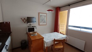 A compact room with a kitchenette, a dining area, a television, and a window with curtains.