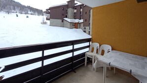 A balcony with a view of a snowy landscape and buildings. There are two white plastic chairs and a table with a white tablecloth.
