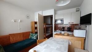 A compact living space with a sofa, a dining table, a kitchenette, and a TV mounted on the wall.