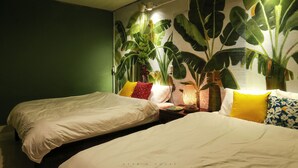 A room with two beds, a green wall, and a large plant mural.