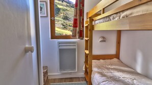 Une petite pièce avec un seul lit superposé, une fenêtre, un radiateur, une échelle en bois et un tapis.