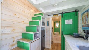 Una cocina compacta con armarios verdes, un refrigerador de acero inoxidable y un lavamanos.